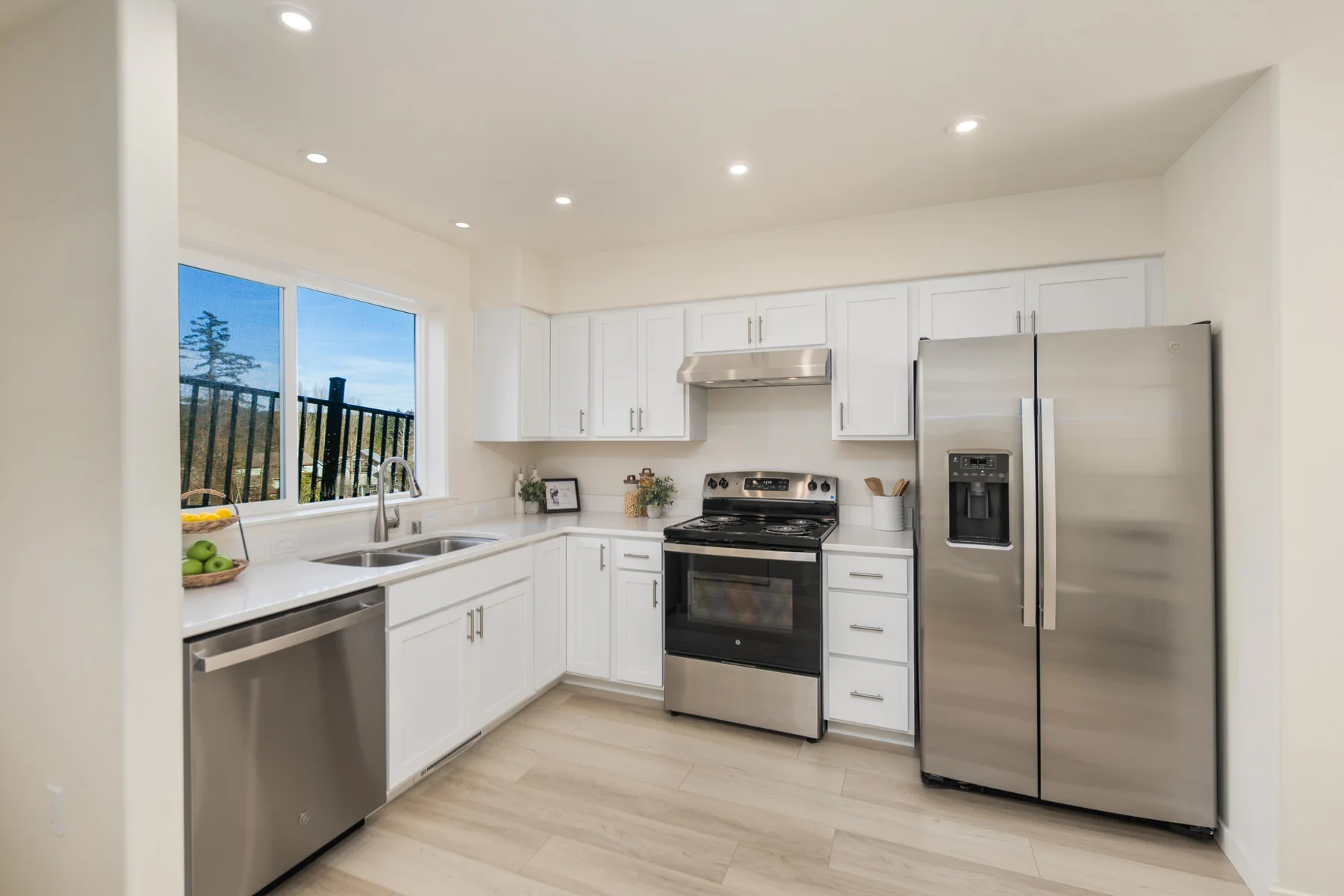 White kitchen cabinetry with stainless steel appliances and a window above the sink